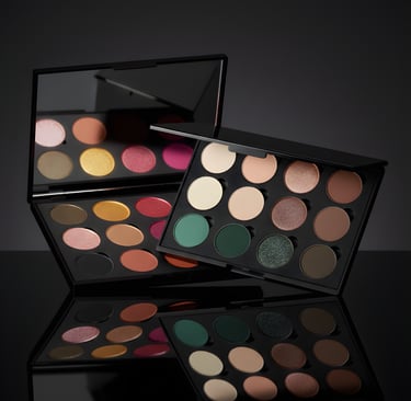Professional eyeshadow palettes with colorful matte and shimmer pans on a reflective black surface.