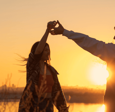 a man and woman dancing at sunset