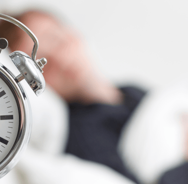 a man laying in bed with a clock on the side of the clock