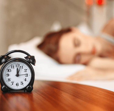 a woman is sleeping in bed with a clock