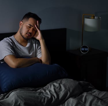 A tired man with insomnia sitting up in bed at night holding his head while suffering from sleep deprivation.