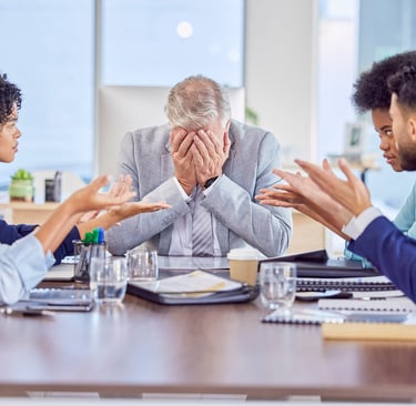 Stressed senior manager covering his face during a tense business meeting with diverse colleagues arguing.