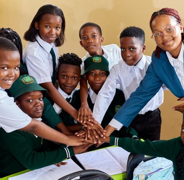 Diverse African students in school uniforms and their teacher stack hands in a classroom team huddle.