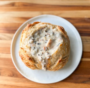 bread bowl on a wooden table with creamy chicken wild rice soup in it.