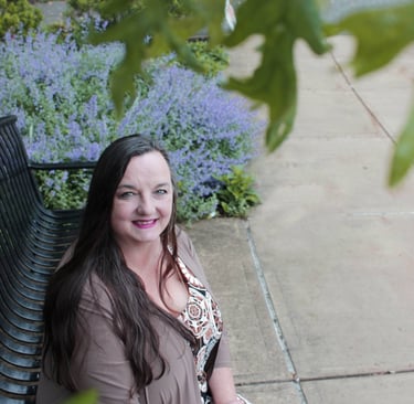 Photo of RuthAnn Lander smiling on a bench under a tree