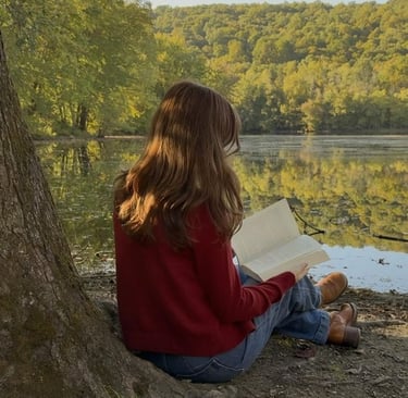 A girl reading a book on the edge of a lake