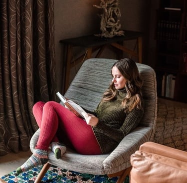 Woman sitting comfortably on a chair in her living room reading a book