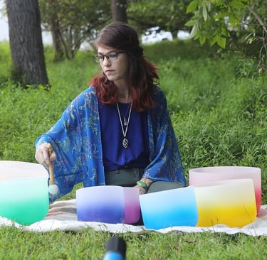 a woman sitting on a blanket playing her crystal singing bowls