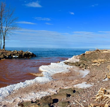 Snow-lined Lake Superior shoreline with blue water and scattered beach rocks