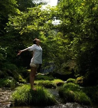 Femme debout en forêt, respirant profondément pour apaiser le stress et se reconnecter à son corps