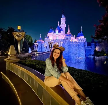 Woman sitting in front of Sleeping Beauty Castle - Disneyland after dark
