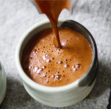Rich hot chocolate being poured into a ceramic mug with frothy bubbles on the surface.