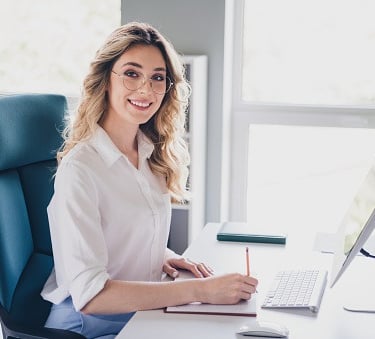 Une femme, secrétaire, assistante administrative, assise à son bureau devant un ordinateur