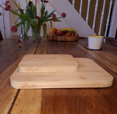 one 8" x 6" bamboo cutting board sat on top of a 12" x 9" bamboo cutting board with Palm-Crafts logos, on a table.