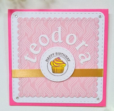 Pink birthday card with white border features "Happy Birthday" text and name "Teodora" and a cupcake