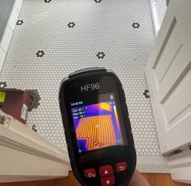 Thermal imaging camera displaying heated floor coils beneath a white and black hexagonal tile bathroom floor.