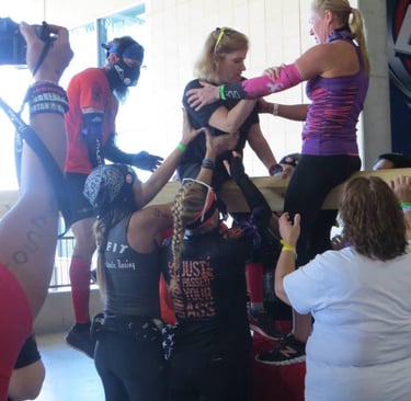 a group of women helping eachother over a wall at an obstacle race