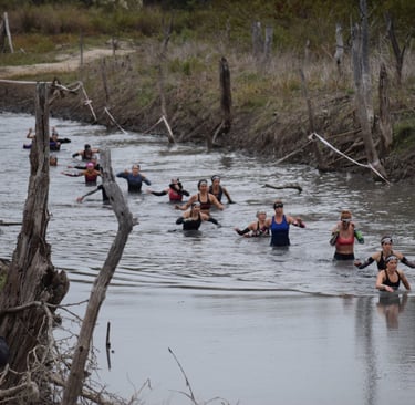 Female elite obstacle racers going through muddy creek obstacle