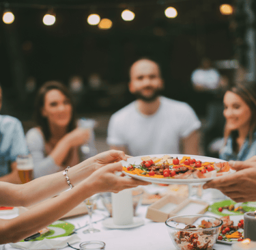 several relaxed happy people are passing beautiful food around a dinner table