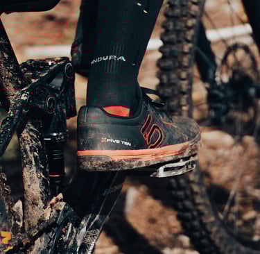 mountain biker wearing Five Ten shoes on flat pedals, covered in mud on a trail