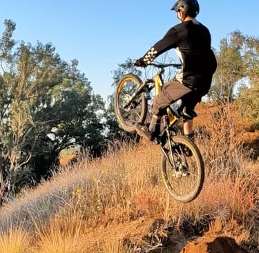 Mountain biker leaning too far back mid-air, about to land rear wheel first on a dirt jump — risk of