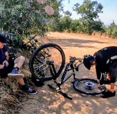 2 mountain bikers with a bike upside down fixing a flat tire