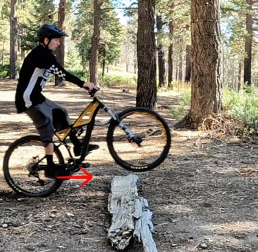 mountain biker pushing rear wheel into a log with feet to do the bump jump