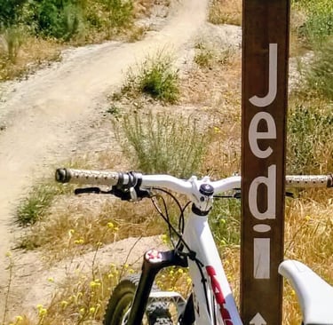  White mountain bike leaning against a blue square trail marker sign on a dirt singletrack trail at 