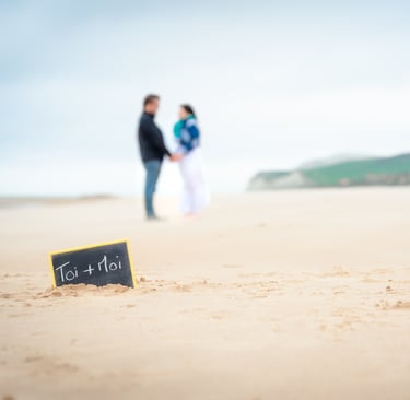 Un couple sur une plage de sable blanc face à face avec une ardoise au premier plan