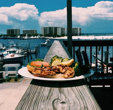 a plate of food on a table with a view of a boat in the background