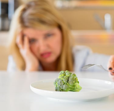 a woman sitting at a table with a plate of broccoli