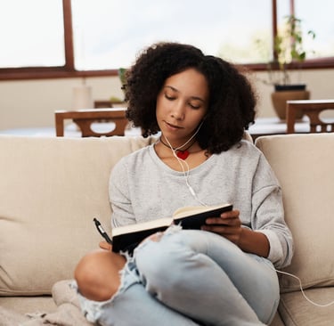 a woman sitting on a couch with headphones journaling in a notebook on