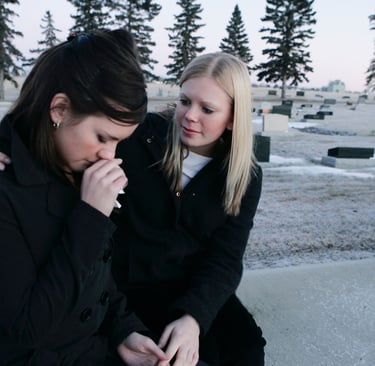 two women sitting on a bench in a cemetery