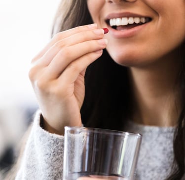 a woman holding a glass of water and taking a vitamin and smiling
