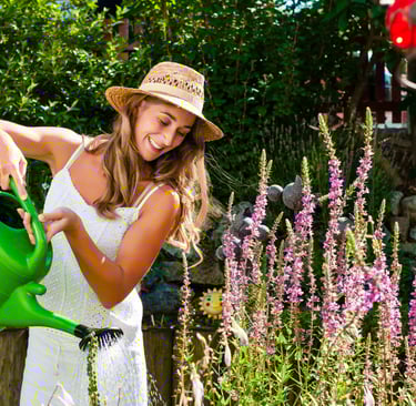 a woman in a white dress and hat is watering the plants