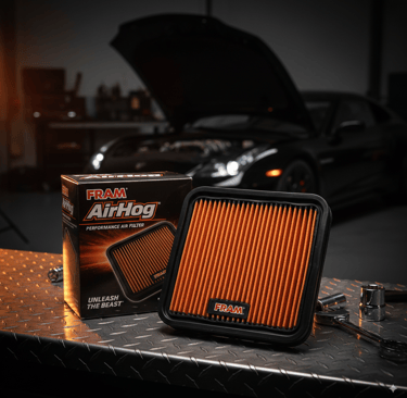 FRAM AirHog performance air filter, orange pleated media, next to its packaging on a metal workbench