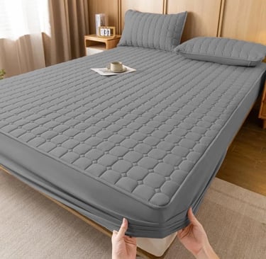 Quilted grey waterproof mattress protector with matching pillow shams on a modern wooden bed frame.