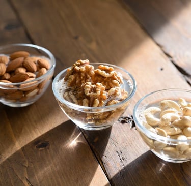 Bodegón de diferentes cuencos de cristal con almendras, nueces y anacardos sumergidos en agua sobre una mesa de madera clara