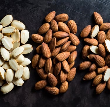 Bodegón comparativo mostrando almendra Marcona redondeada, Largueta alargada y Comuna sobre una mesa de madera - Raw Rico