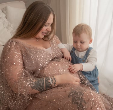 A pregnant mother in a sequin maternity gown sitting with her toddler during a maternity photoshoot.