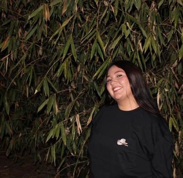 A smiling young woman in a black t-shirt posing in front of lush green bamboo leaves at night.
