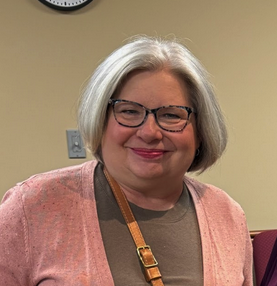 Woman with gray hair and glasses smiling.