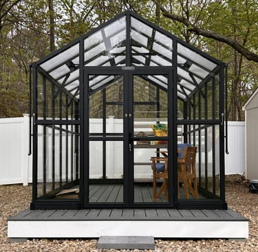 Front view of an assembled Vego Victorian greenhouse with black metal, glass side panels and polycarbonate roof panels.