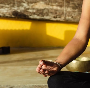 Close-up of yoga teacher seated in Gyan mudra against yellow background, everyday essentials