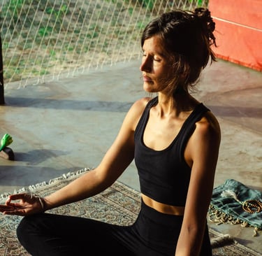 Woman meditating on yoga mat in afternoon sun inside yoga shala, online meditation coaching