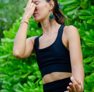 Yoga teacher practicing Nadi Shodhana pranayama seated in nature, everyday essentials