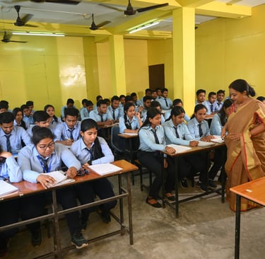 Students studying in a classroom with a lady teacher guiding them.