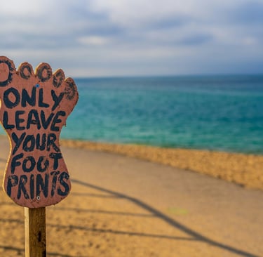 A foot shaped board 'only leave your foot prints written on it' in the backdrop of a sea.