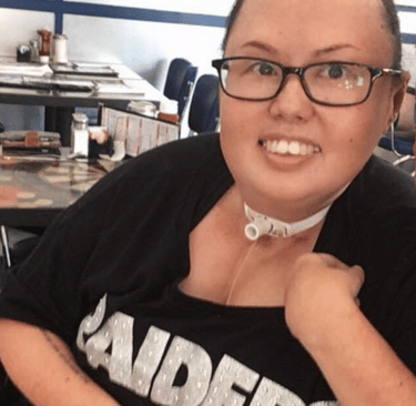Photo of Stacey with hair pulled back and smiling with a Raiders tee shirt.