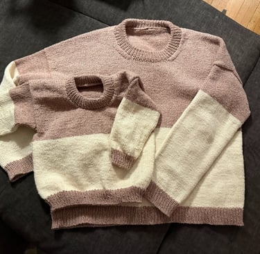 Hand-knitted matching adult and child color-block sweaters in dusty rose and cream wool yarn.